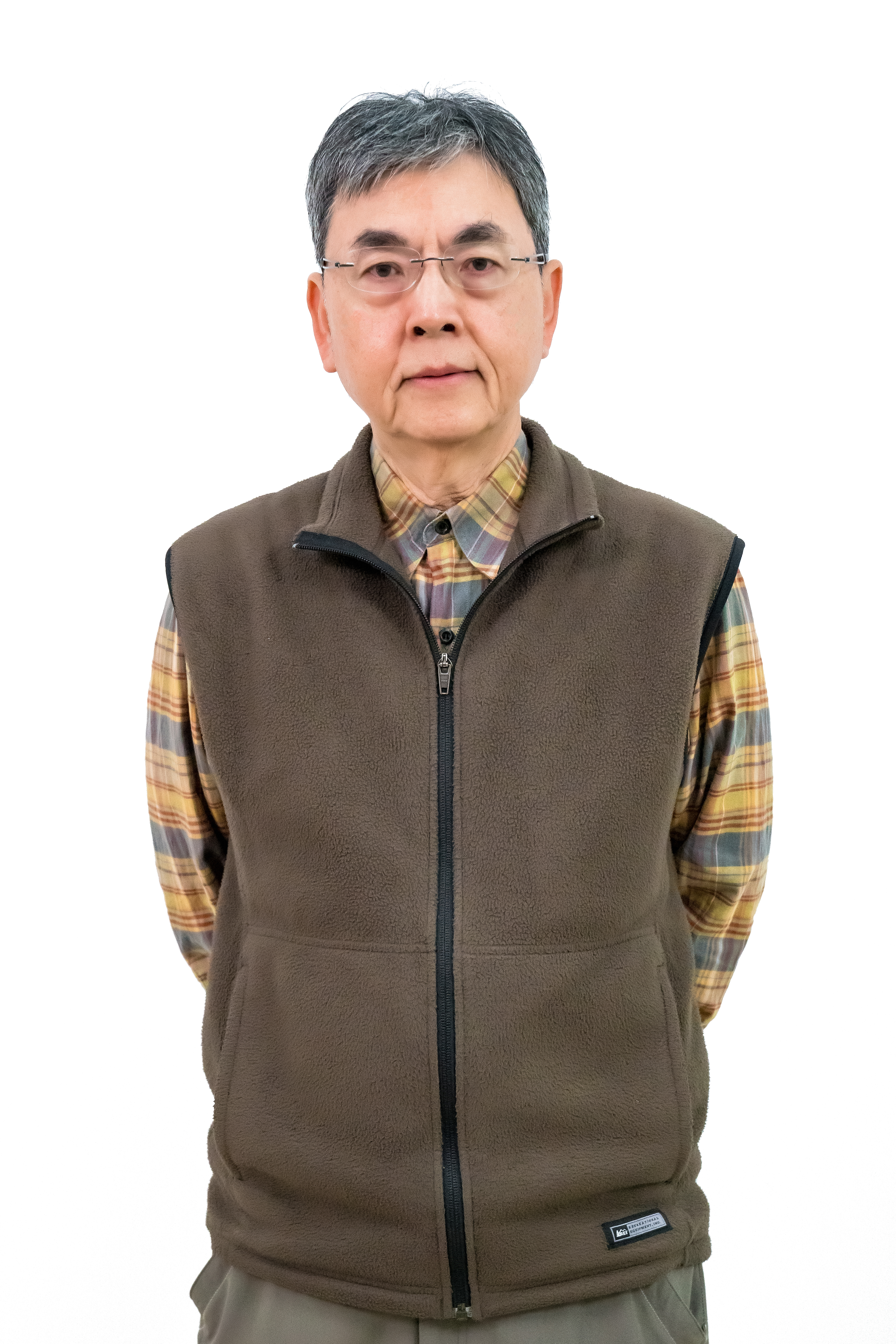 照片中是一位中年男性，他穿著格子襯衫和棕色背心，表情沉穩。背景為純白色，增強了整體的簡約感。他的眼鏡和灰白色頭髮增添了一份智慧感。
